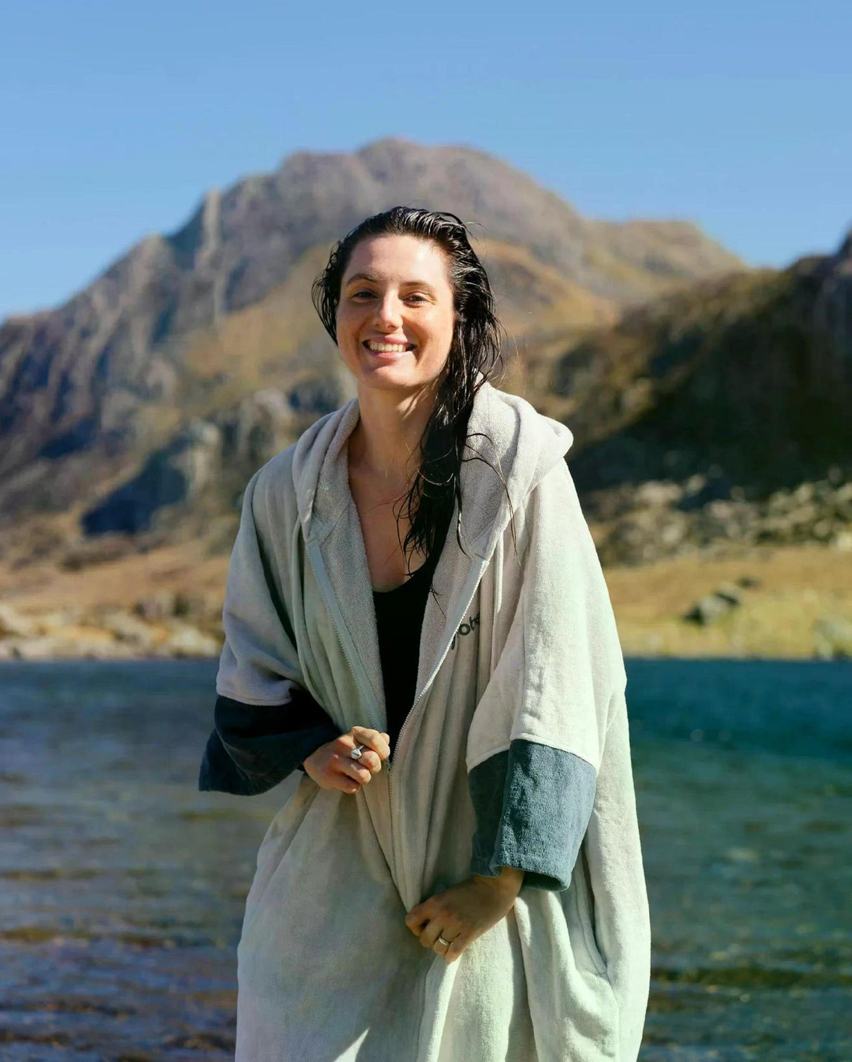 Dryrobe Fullzip Handtuchmantel aus Bio-Baumwolle in Creme, getragen am See mit Bergen im Hintergrund