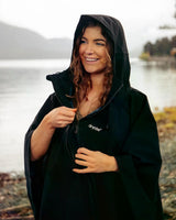 Dryrobe Regen-Poncho in Schwarz, wasserdicht, mit Kapuze, getragen von einer Frau am See