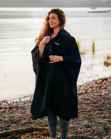 Frau trägt schwarzen Dryrobe Regen-Poncho am Strand, wasserdicht, Frontalansicht