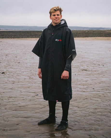 DRYROBE Advance Kurzarm Bademantel in Schwarz mit Kapuze, getragen am Strand, Frontalansicht