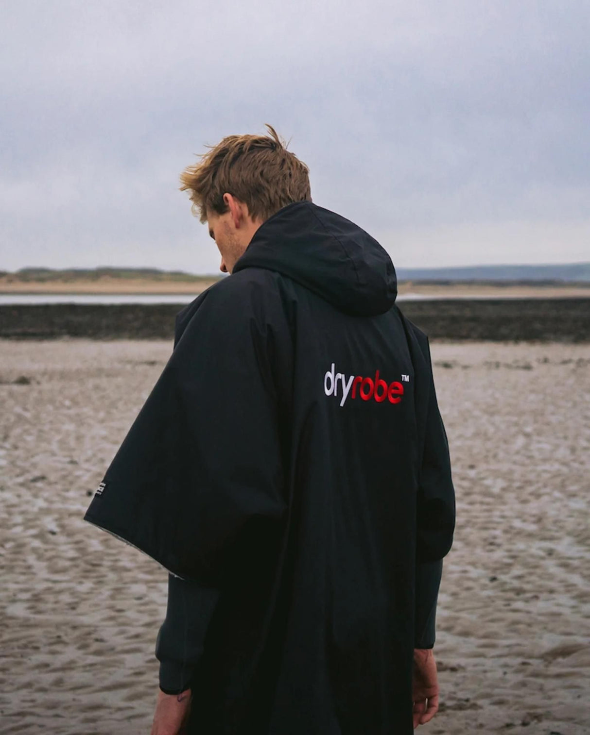 DRYROBE Advance Kurzarm Umhang in Schwarz, Rückansicht am Strand getragen