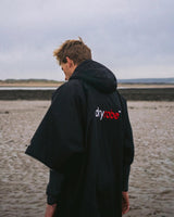 DRYROBE Advance Kurzarm Umhang in Schwarz mit Logo, von hinten am Strand getragen