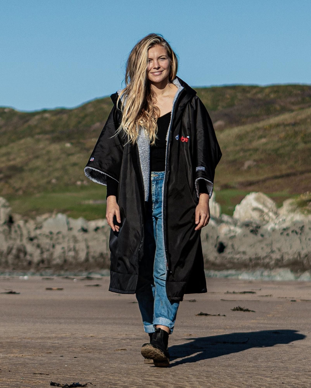 DRYROBE Advance Kurzarm in Schwarz, Frau trägt Umhang am Strand, Frontalansicht