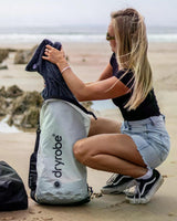 Dryrobe wasserdichter Packsack Drybag in Grau-Schwarz, geöffnet am Strand, Frau demonstriert Verwendung