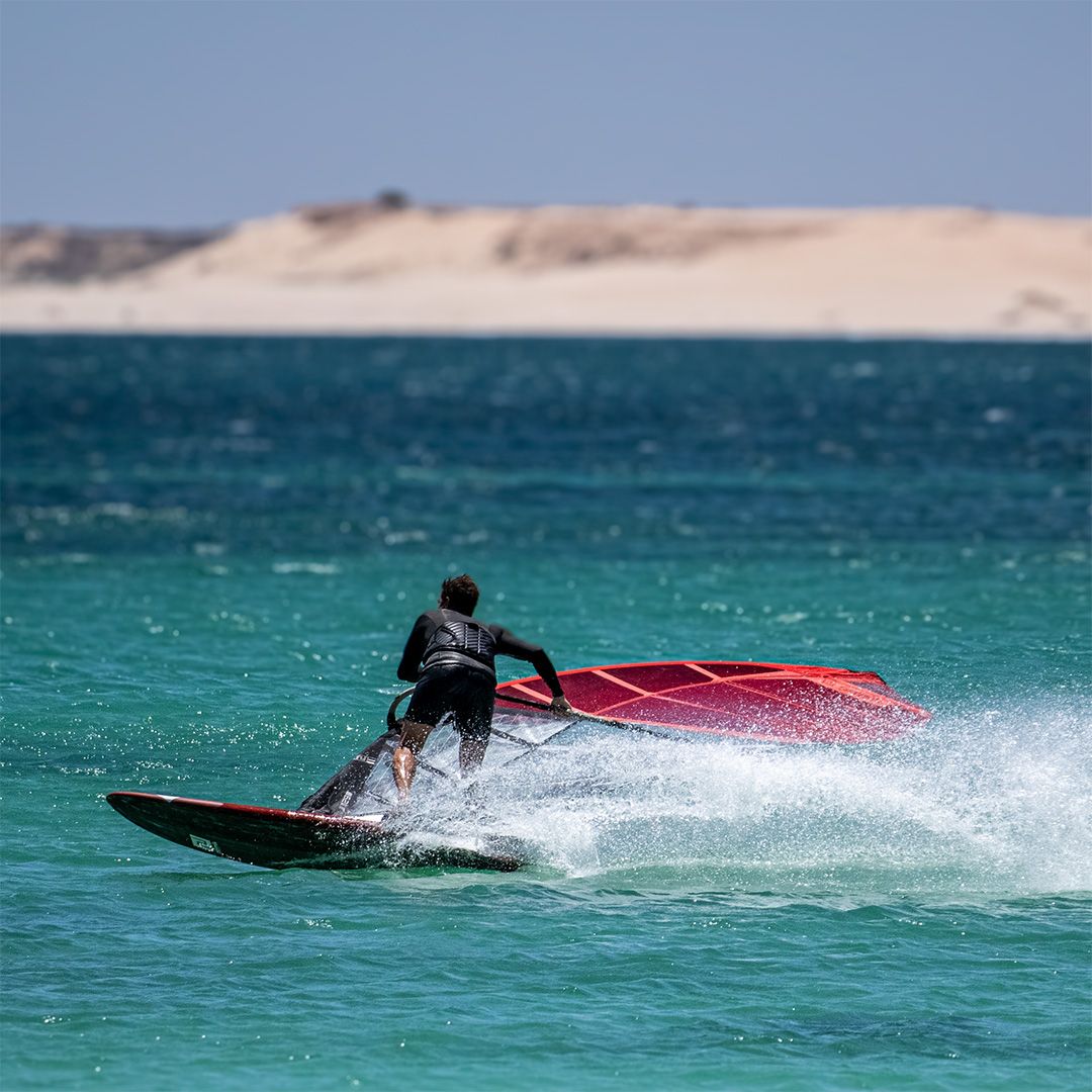 Patrik Slalom-X Windsurfboard in Schwarz und Rot, Fahrer in Aktion auf türkisem Wasser mit rotem Segel