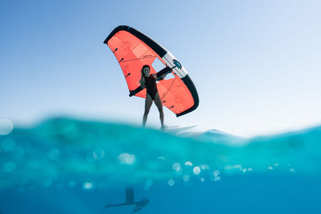 Duotone Unit 2027 Kite in Rot-Schwarz, Kitesurfer hält Lenkdrachen über Wasser, Frontalansicht