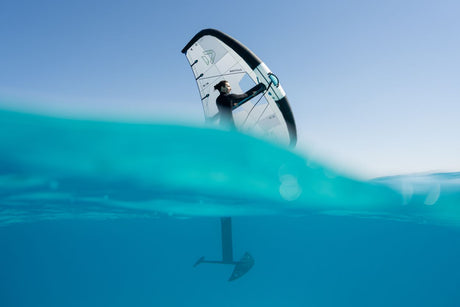 Duotone Unit 2027 Kiteboard weiß-blau mit Fahrer auf türkisblauem Wasser, Split-View Unterwasserperspektive