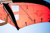 Duotone Unit 2027 Kitesegel rot-orange mit schwarzem Rahmen und Griffschlaufen, Frontalansicht gegen blauen Himmel