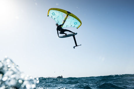 Duotone Unit D/LAB 2027 Kiteboard mit grün-gelbem Tuch, Kitesurfer in Sprungposition über Wasser, Frontalansicht