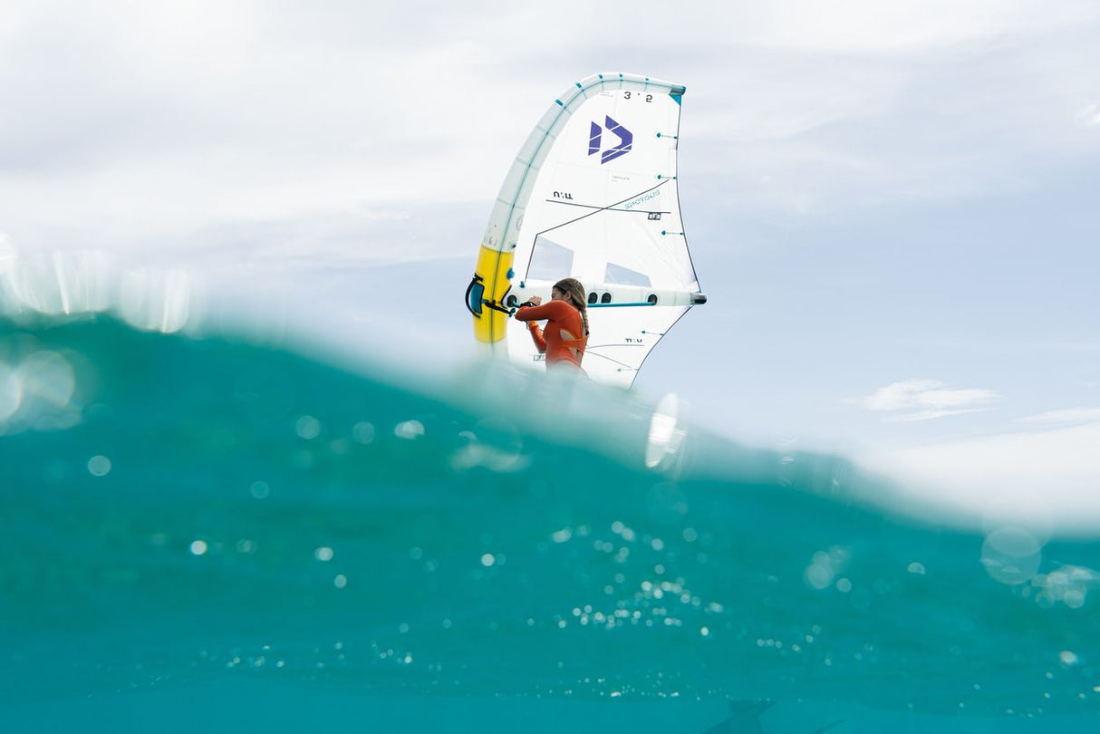Duotone Unit SLS 2027 Windsurfboard weiß-blau mit Segel auf türkisem Wasser, Frontalansicht