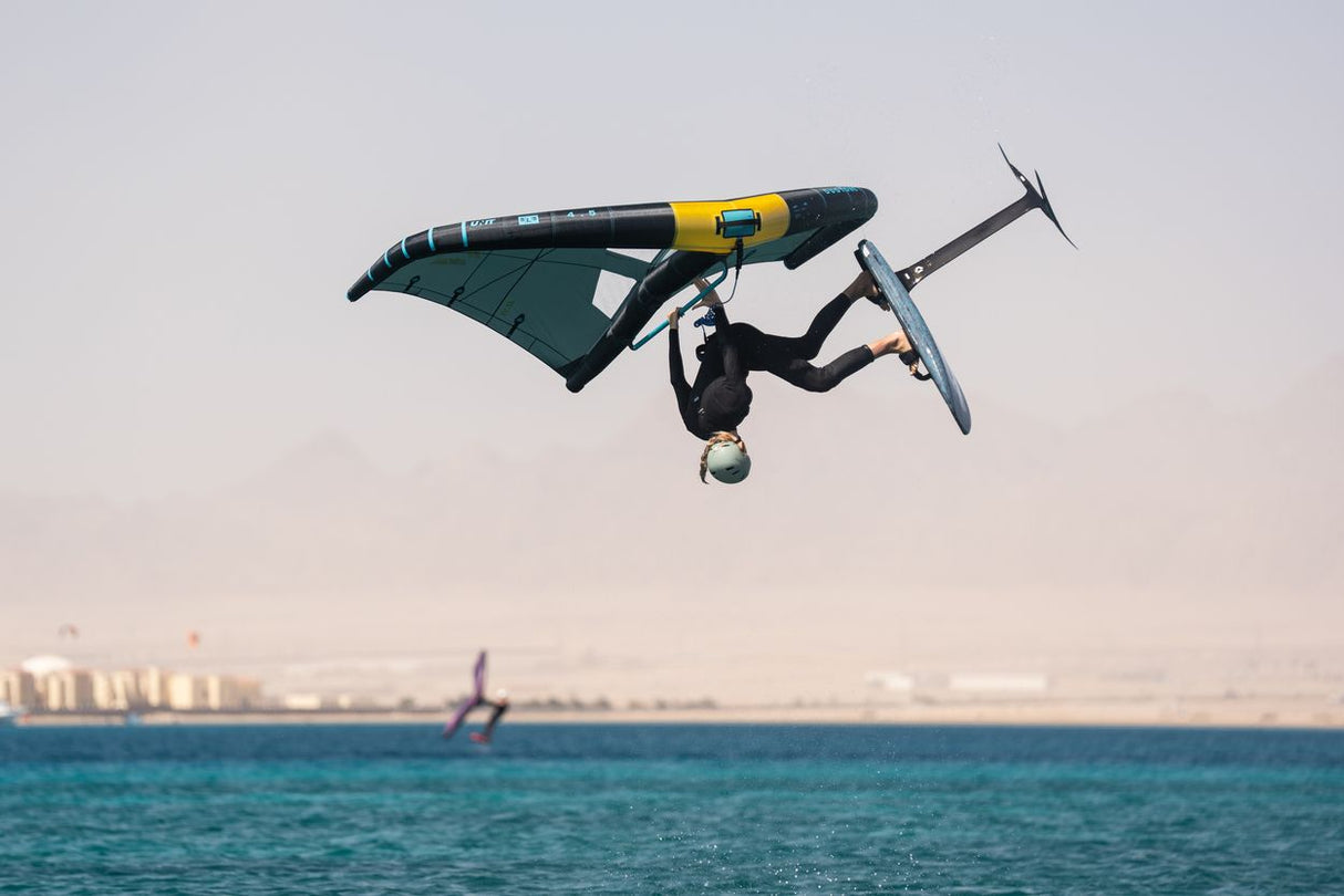 Duotone Unit SLS 2027 Kite in Dunkelblau und Gelb, Athlet in Flugposition über Wasser während Kiteboarding-Trick