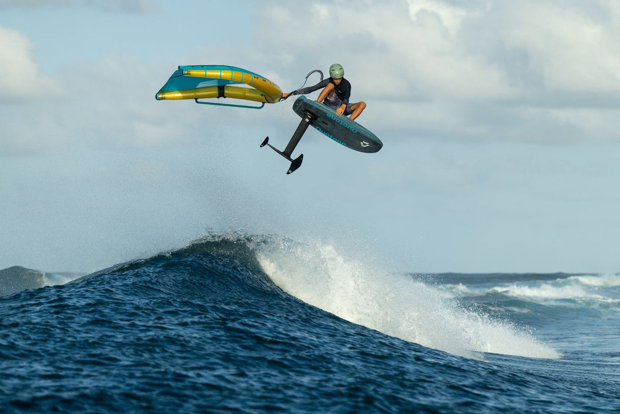 Duotone Sky Style SLS 2027 Kiteboard mit blauem und gelbem Design in Aktion über Welle, Sportperspektive