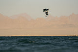 Duotone Sky Style SLS 2027 Kiteboard in Schwarz-Blau, Athlet in Aktion über Wasser mit Bergen im Hintergrund