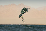 Duotone Sky Style SLS 2027 Kiteboard in Dunkelgrün und Beige, Sprung über Wasser mit Bergkulisse, Seitenansicht