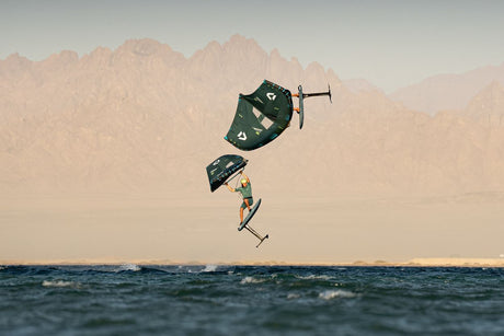 Duotone Sky Style SLS 2027 Kiteboard in Dunkelgrün und Beige, Sprung über Wasser mit Bergkulisse, Seitenansicht
