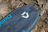 Duotone Sky Style SLS 2027 Kiteboard mit dunkelblauem Deck, weißem Logo und türkisen Beschriftungen im Sand