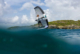 Duotone Sky Style 2027 Kiteboard in Grau-Weiß, Athlet in Action über türkisblauem Wasser mit Klippen im Hintergrund