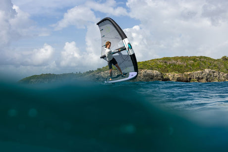 Duotone Sky Style 2027 Kiteboard in Grau-Weiß, Athlet in Action über türkisblauem Wasser mit Klippen im Hintergrund