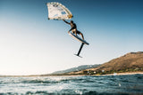 Duotone Sky Style 2027 Kiteboard weiß-blau, Athlet in Sprung über Meer mit Landschaft im Hintergrund