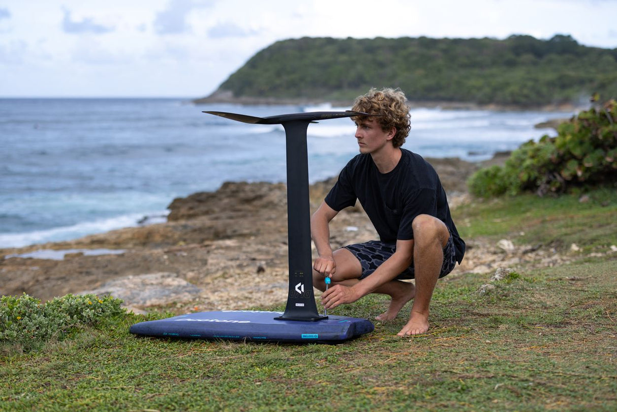 Duotone Crush SLS 2027 Kiteboard mit blauem Deck und schwarzem Gestell, Person beim Setup am Strand