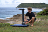 Duotone Crush SLS 2027 Kiteboard mit blauem Deck und schwarzem Gestell, Person beim Setup am Strand