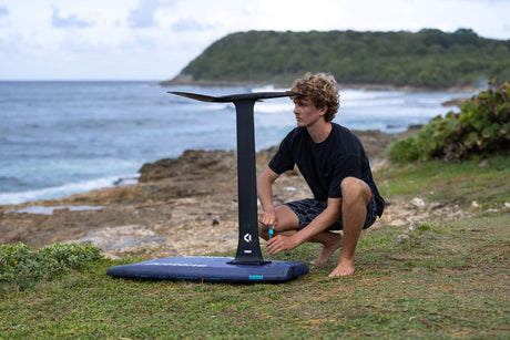 Duotone Crush SLS 2027 Kiteboard mit blauem Deck und schwarzem Gestell, Person beim Setup am Strand