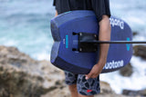 Duotone Crush SLS 2027 Kiteboard in Blau-Schwarz, von vorne gehalten an Strand mit Wellen