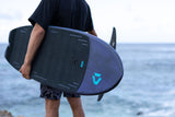 Duotone Crush SLS 2027 Kiteboard in Dunkelblau und Schwarz, von Person am Strand gehalten, Meeresansicht