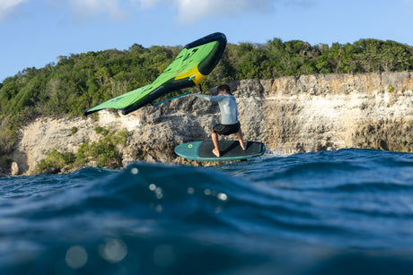 Duotone Skybrid SLS 2027 Kite in Grün-Gelb, Wassersportler beim Kiteboarden mit Klippe im Hintergrund