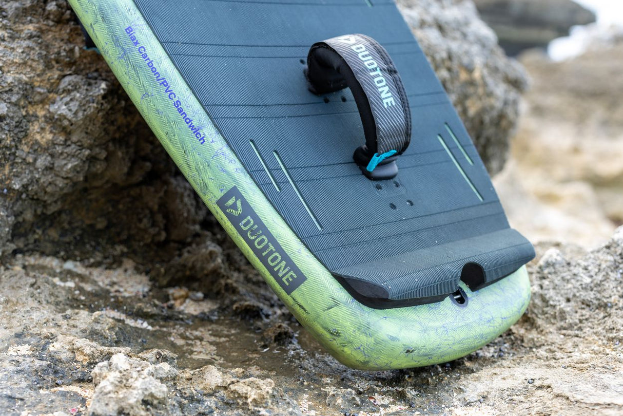 Duotone Trace SLS 2027 Kiteboard mit blauem Deck, grünem Rail und schwarzem Kontrollelement, Draufsicht auf Stein