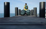 Duotone Combibag 2027 Reisetasche in Grün und Grau, Person mit Rucksack am Steg mit Meerwasser im Hintergrund