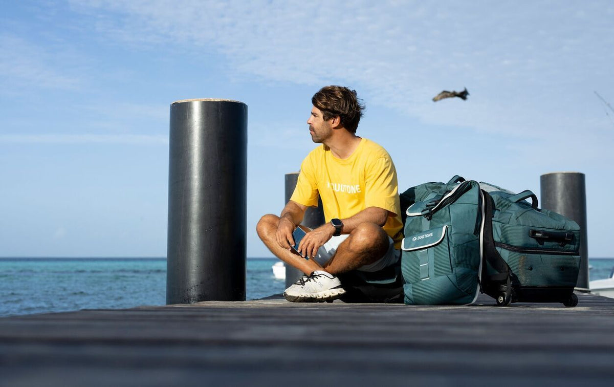 Duotone Combibag 2027 in Grün-Blau neben einer Person am Meer, Seitenansicht der Reisetasche