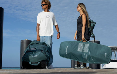 Duotone Team Bag 2027 Kitesportausrüstung in Grün und Schwarz, von zwei Personen am Strand getragen
