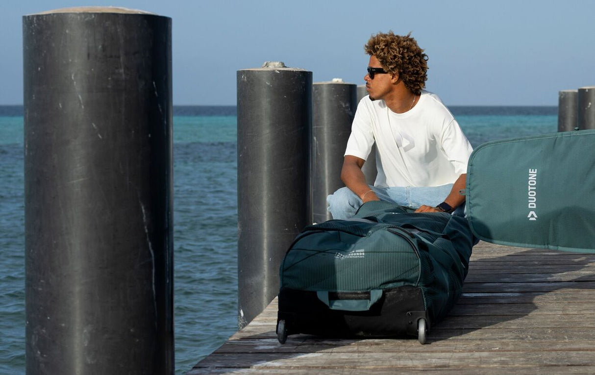 Duotone Team Bag 2027 Sporttasche in Dunkelblau und Grün, Person sitzt auf Steg am Meer