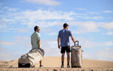 Duotone Team Bag 2027 Reisetasche in Beige und Grau, von zwei Personen in Wüstenlandschaft getragen