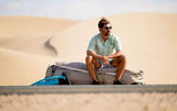 Duotone Boardbag Single Compact 2027 in Grau und Blau, Mann sitzt darauf in Wüstenlandschaft
