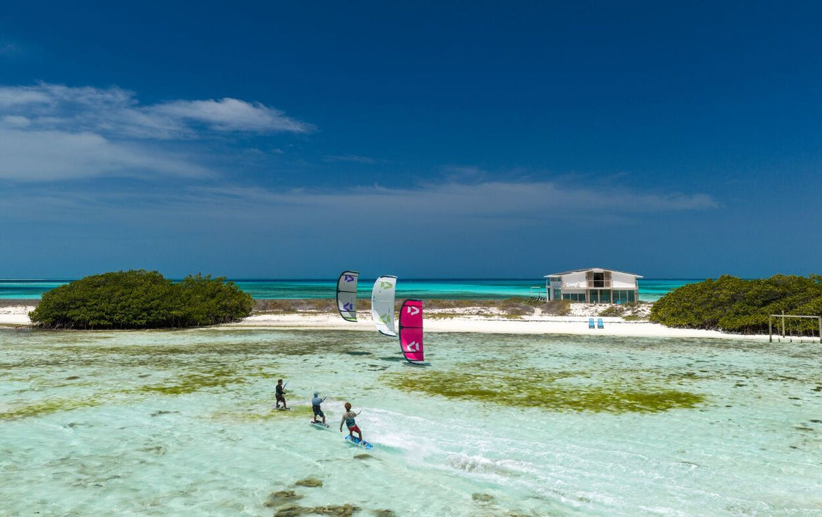 Duotone Entity Ergo 2027 Kiteboard in Pink und Weiß, Lagune mit Kitesurfern und Strandanlage