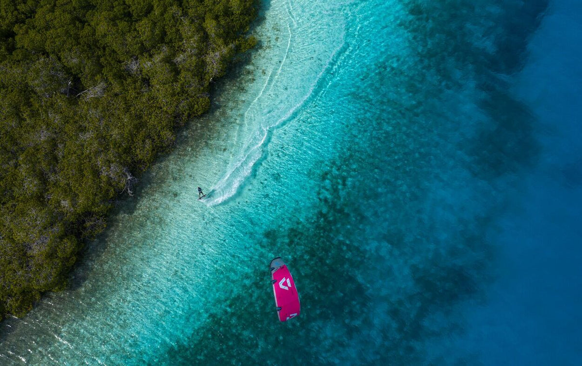 Duotone Entity 360 2027 Kiteboard pink, Luftaufnahme über türkisblauem Wasser und grüner Küste