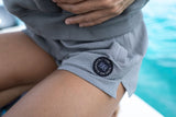 ION Tally 2.5 Boardshorts Damen grau, getragen am Wasser, Detail des Logos sichtbar