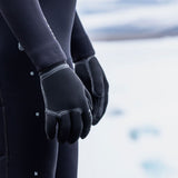 ION Neo Gloves 4/2 2026 Neopren-Handschuhe in Schwarz, getragen an Händen, Detailansicht mit Wasser im Hintergrund