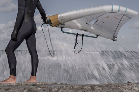ION Windsurf Harness Line Vario 2026 in Schwarz, Frontalansicht mit Windsurfboard am Strand