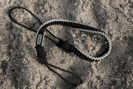 ION Uphaul Line TEC 2026 schwarze Trapezleine mit weißem Elastikband und Handschlaufe auf Sand, Draufsicht