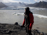 ION Fuse Lightweight Drysuit Back Zip 2026 in Schwarz und Rot, getragen am Strand mit Gletscherlandschaft im Hintergrund