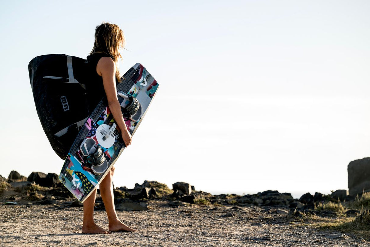 ION Suspect Duffel Bag 2024 schwarz, Kitesportler trägt Tasche, Strandszene