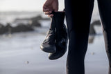 ION Ballistic Boots 3/2 schwarze Neopren-Stiefel mit Split-Sohle, in Hand gehalten, Strandkulisse