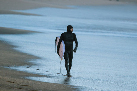 ION Ballistic Boots 3/2 Round Toe schwarz, Surfer am Strand mit Neoprenanzug und Surfboard, Ansicht von vorne