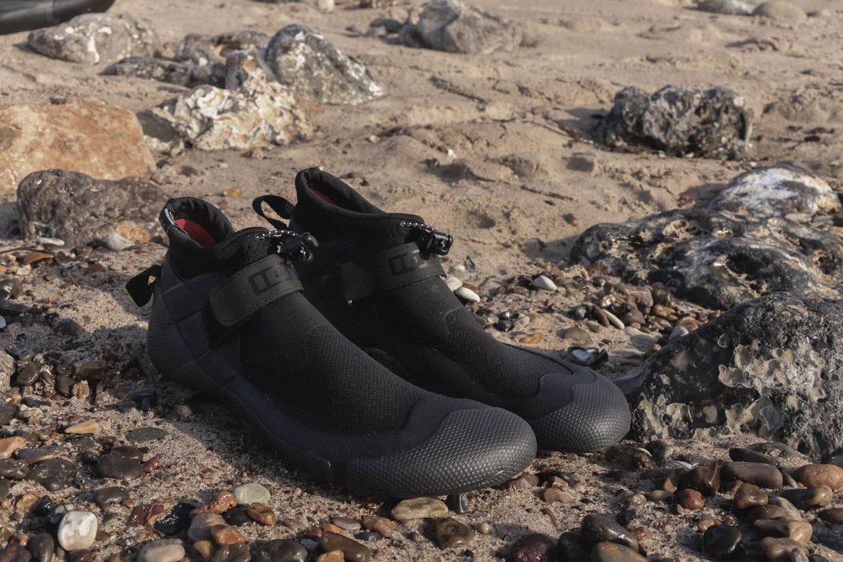 ION Ballistic Shoes 2.5 Round Toe 2026 schwarze Wassersportschuhe mit Neoprenmaterial auf steinigem Strand, Seitenansicht