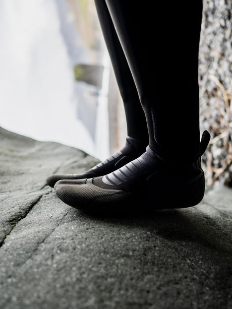 ION Plasma Boots 3/2 Internal Split schwarz, getragen auf Stein, Detailansicht Sohle und Ferse