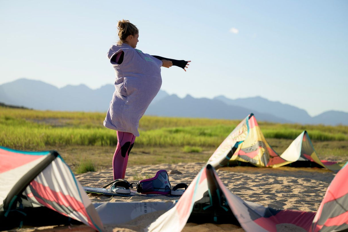 ION Poncho Core 2026 Fliegerponcho in Lila, tragbar beim Kitesurfen, flache Perspektive am Strand