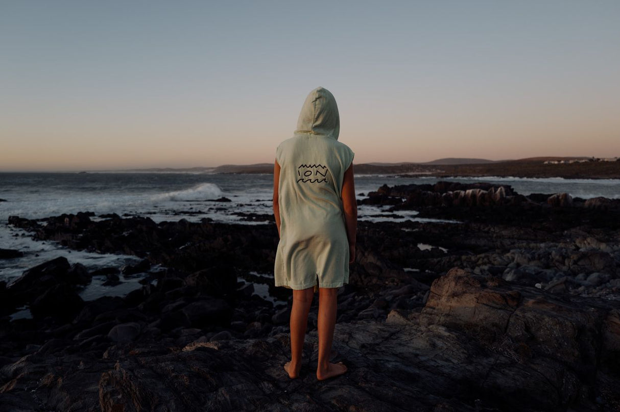 ION Grom 2025 Poncho in Creme mit roten Ärmeln, Rückansicht am Strand